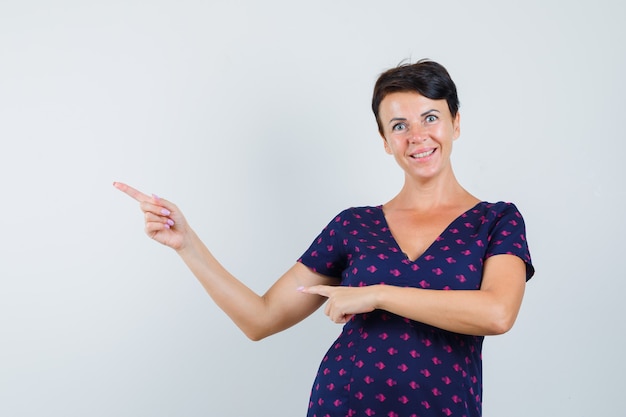 Vrouw wijzend op de linkerbovenhoek in jurk en ziet er vrolijk uit.