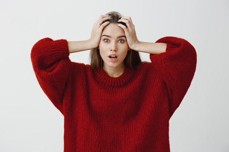 Gratis Foto vrouw wist niet hoe ze het probleem moest oplossen, omdat ze zich zorgen maakte. benadrukt geschokte mooie vrouw in stijlvolle rode losse trui, hand in hand op het hoofd, nerveus geconfronteerd met problemen over grijze muur