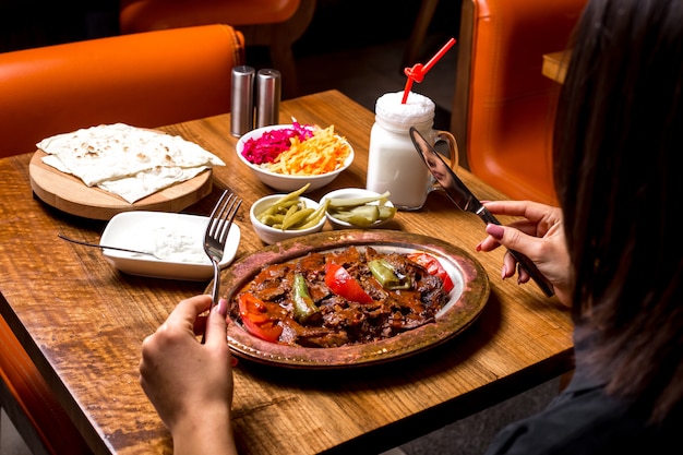 Vrouw wordt iskender kebab geserveerd in koperen schaal met augurken, yoghurt en ayran