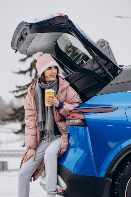 Vrouw zit in de kofferbak van haar auto koffie te drinken