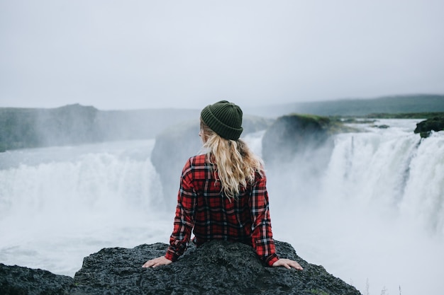 Vrouw zit op de rand van de klif op de waterval