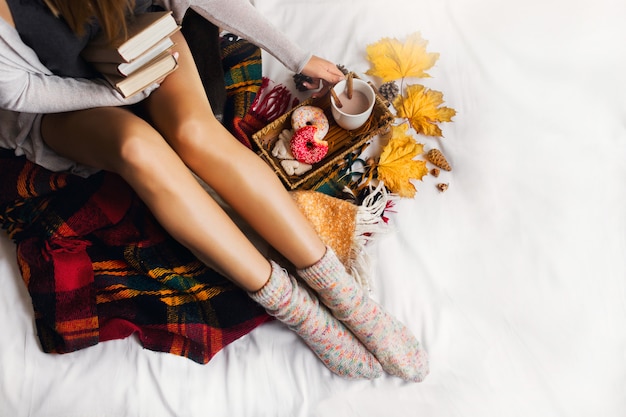 Vrouw zitten in haar bed met boeken en koffie drinken met kaneel, koekjes en geglazuurde donuts.