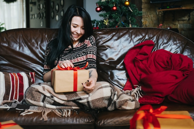 Gratis foto vrouw zittend op de bank met een deken en een geschenk