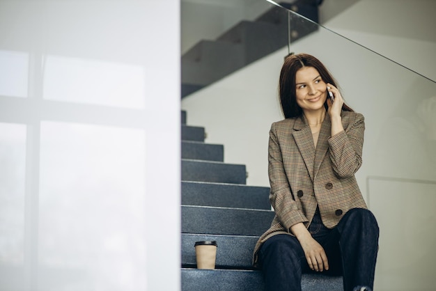 Vrouw zittend op de trap koffie drinken en telefoon gebruiken