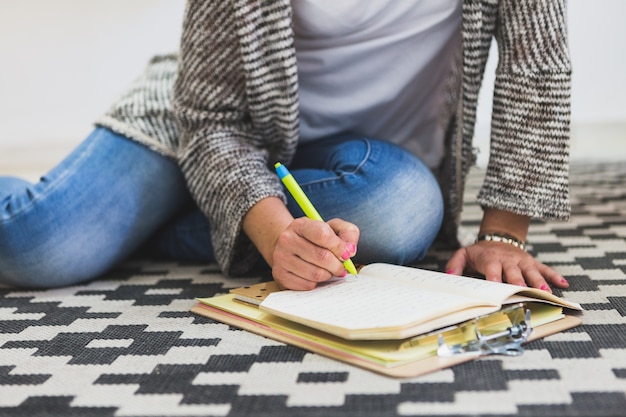 Gratis foto vrouw zittend op de vloer en schrijven in haar notitieboekje