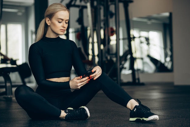 Vrouw zittend op de vloer in de sportschool en het gebruik van mobiele telefoon