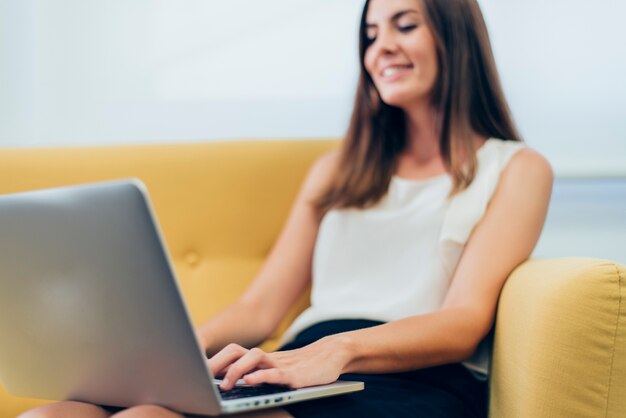Vrouw zittend op een bank met een laptop op de benen en lachend