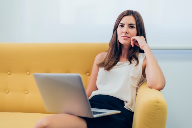 Vrouw zittend op een bank met een laptop op de benen