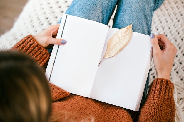 Vrouw zittend op een gebreid tapijt met een gouden knapperig blad op een open notebook