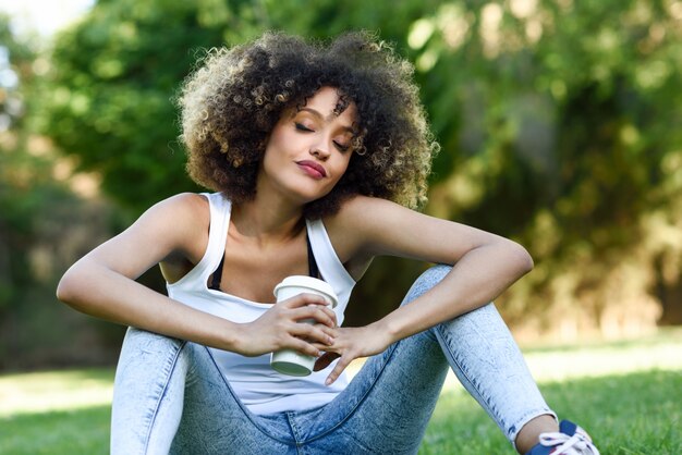 Vrouw, zittend op het gras lachend met een kopje koffie