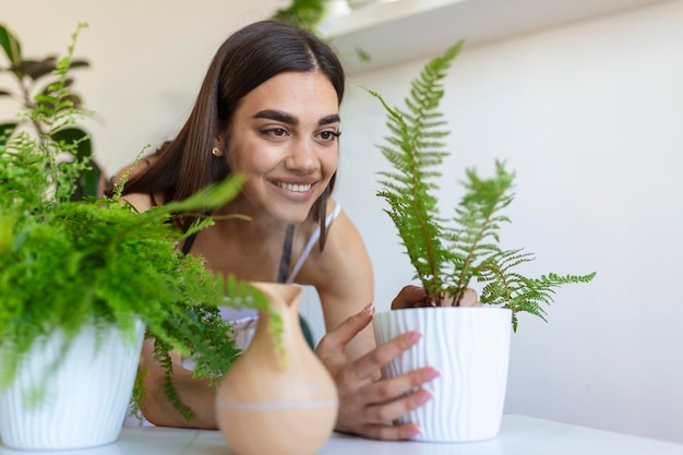 Vrouw zorgt voor planten naast stoomaroma-olieverspreider op tafel thuis stoom van luchtbevochtiger Bevochtiging van lucht in appartement tijdens de periode van zelfisolatie als gevolg van een pandemie van het coronavirus