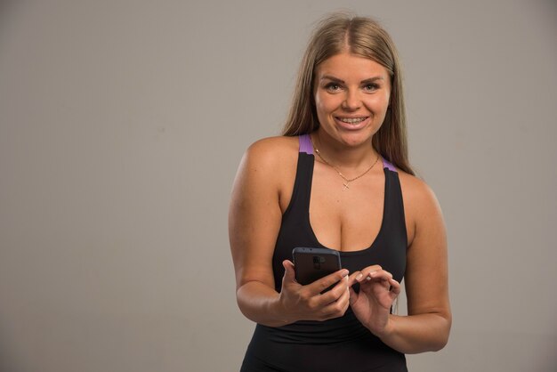Vrouwelijk model in sportbeha texting met haar smartphone.