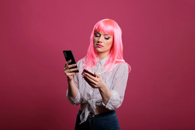 Vrouwelijk model met roze haar met creditcard of betaalpas en smartphone voor het online winkelen van kleding. Geldtransactie doen om te kopen op internetwebsite, met behulp van de app voor mobiele telefoons.