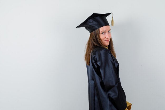 Vrouwelijke afgestudeerde camera in academische kleding kijken en verstandig op zoek.