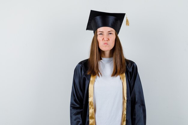 Vrouwelijke afgestudeerde camera kijken terwijl fronsen gezicht in uniforme, vrijetijdskleding en koppig op zoek. vooraanzicht.