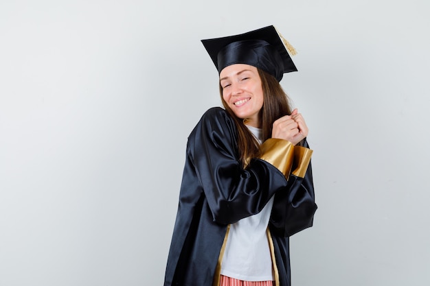 Vrouwelijke afgestudeerde poseren met handen bij elkaar gehouden in uniforme, vrijetijdskleding en op zoek vrolijk, vooraanzicht.