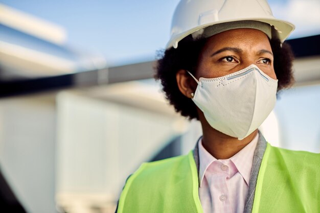 Vrouwelijke Afro-Amerikaanse burgerlijk ingenieur met beschermend gezichtsmasker op bouwplaats