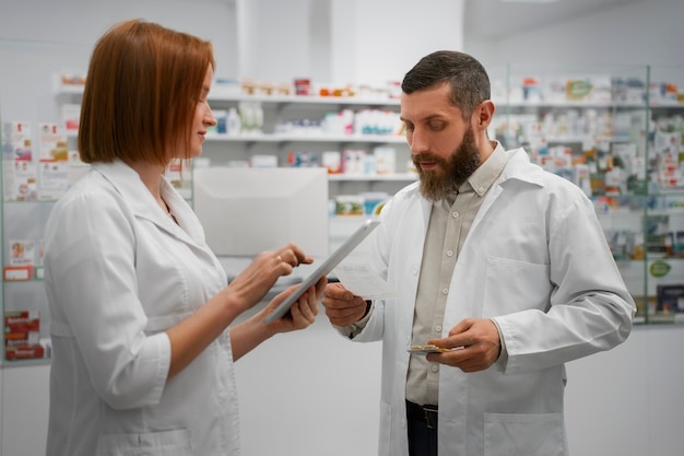 Gratis foto vrouwelijke apotheker die mannelijke collega opleidt met tablet in de apotheek