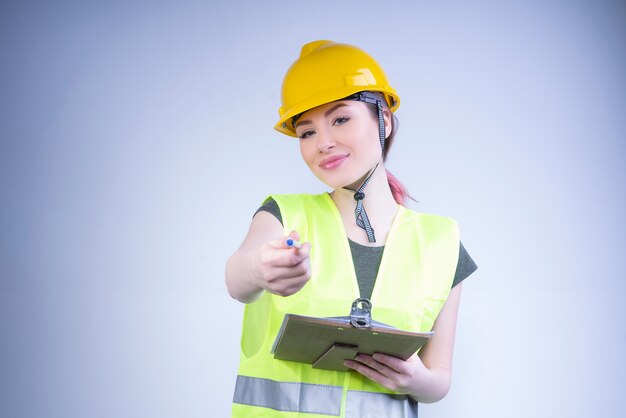 Vrouwelijke architect in een gele helm wijst naar voren met haar pen