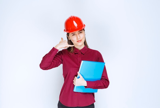 Vrouwelijke architect in rode helm met blauwe map en poseren voor de camera.