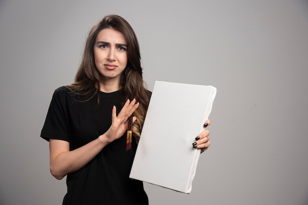 Vrouwelijke artiest in zwart shirt poseren met penseel en canvas.