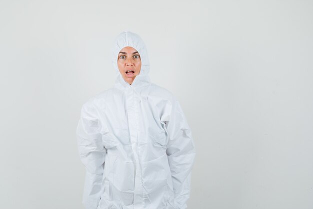 Vrouwelijke arts camera in beschermend pak kijken en geschokt kijken