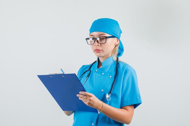 Vrouwelijke arts die aantekeningen op klembord in blauw uniform maakt