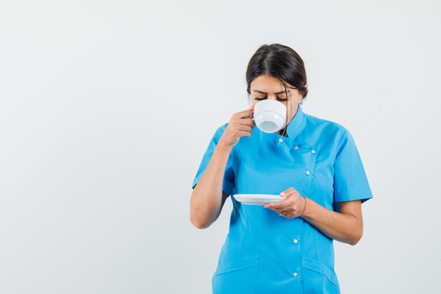 Vrouwelijke arts die aromatische thee drinkt in blauw uniform en er opgetogen uitziet