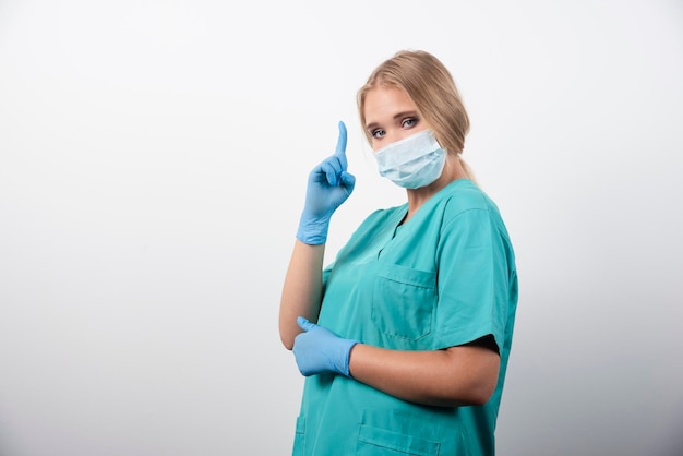 Vrouwelijke arts die duim toont en een medisch masker draagt. Hoge kwaliteit foto