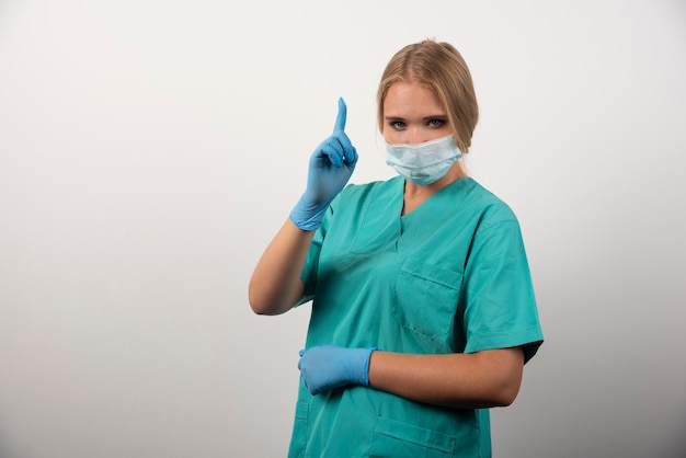 Vrouwelijke arts die duim toont en een medisch masker draagt.
