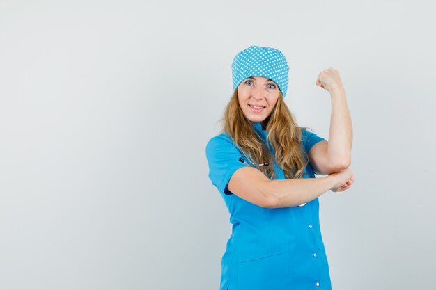Vrouwelijke arts die gebalde vuist in blauw uniform toont en vrolijk kijkt.