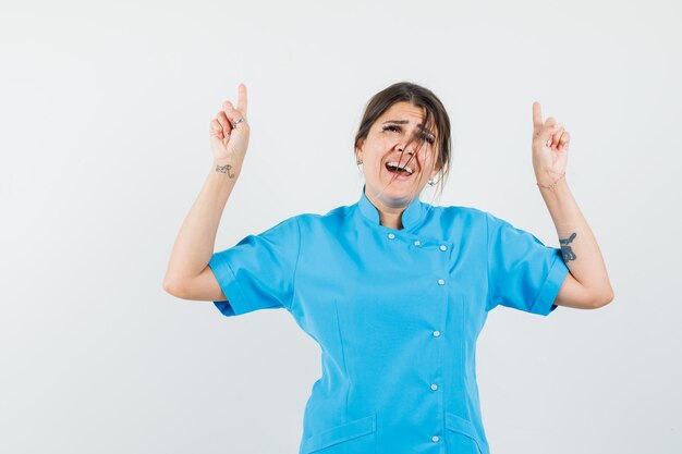 Vrouwelijke arts die in blauw uniform omhoog wijst en er gelukkig uitziet