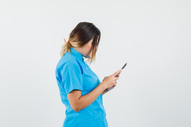 Vrouwelijke arts die mobiele telefoon in blauw uniform gebruikt en er druk uitziet