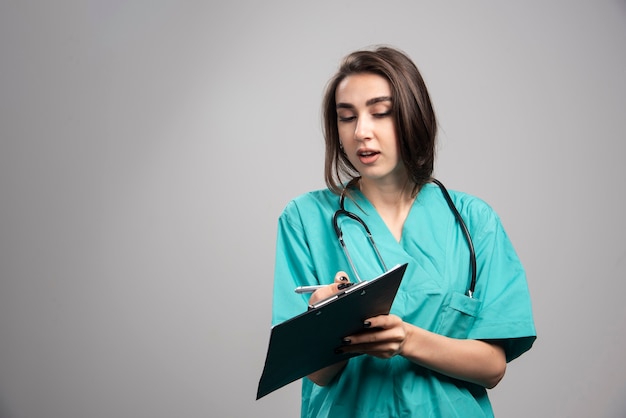 Vrouwelijke arts die nota's over grijze achtergrond toont. Hoge kwaliteit foto