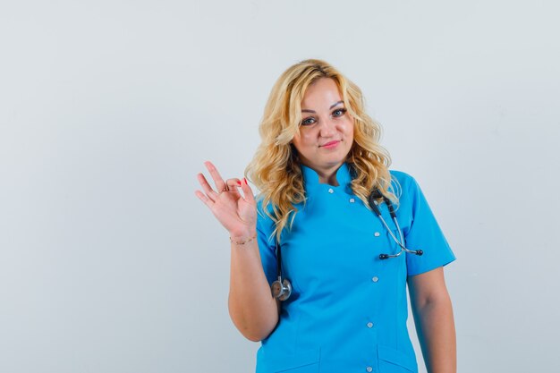 Vrouwelijke arts die ok gebaar in blauw uniform toont en tevreden kijkt