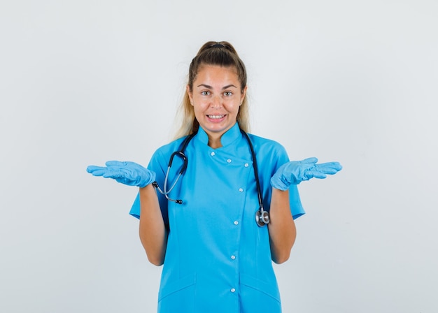 Gratis foto vrouwelijke arts die open handpalmen in blauw uniform opheft