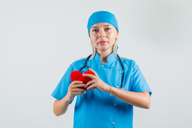 Vrouwelijke arts die rood hart houdt en in blauw uniform glimlacht