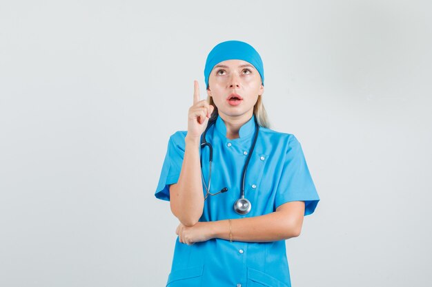 Vrouwelijke arts die vinger in blauw uniform benadrukt en gericht kijkt.