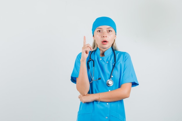 Vrouwelijke arts die vinger in blauw uniform benadrukt en streng kijkt.