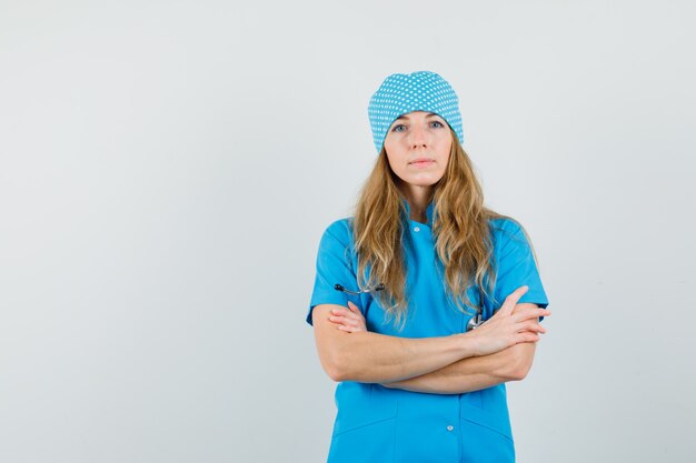 Vrouwelijke arts die zich met gekruiste wapens in blauw uniform bevindt en ernstig kijkt.