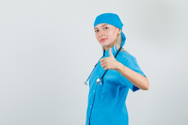 Vrouwelijke arts duim opdagen in blauw uniform en op zoek vrolijk.