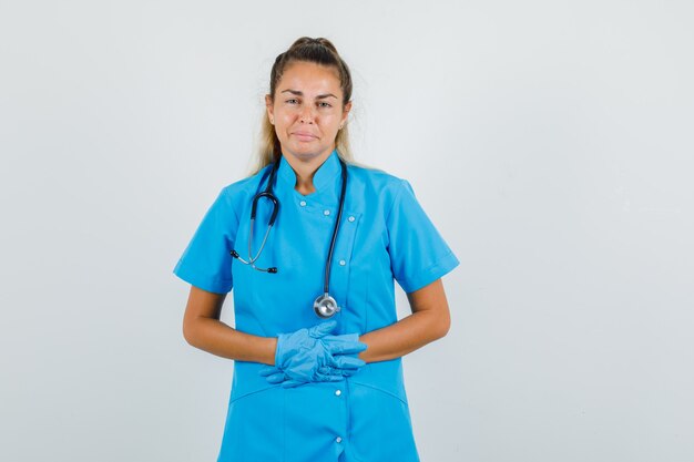 Vrouwelijke arts hand in hand op buik in blauw uniform, handschoenen en op zoek pijnlijk.