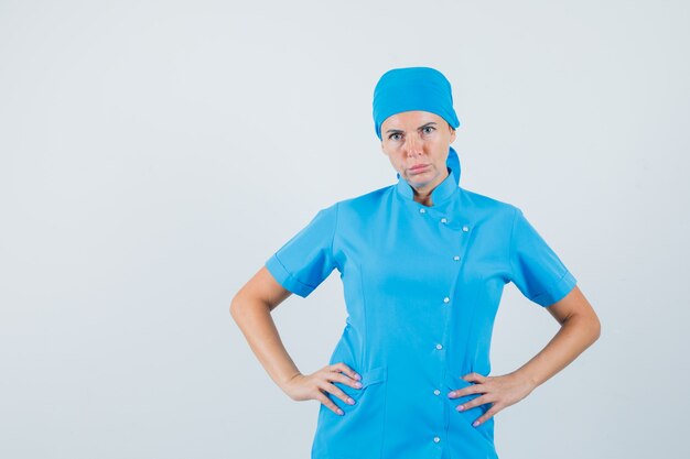 Vrouwelijke arts hand in hand op taille in blauw uniform en op zoek naar ernstige, vooraanzicht.