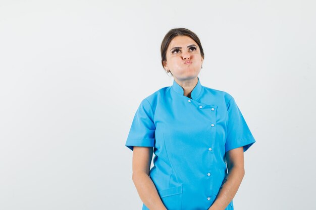 Vrouwelijke arts in blauw uniform blaast op de wangen en ziet er somber uit