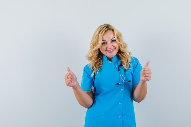 Vrouwelijke arts in blauw uniform die duim toont en blij kijkt