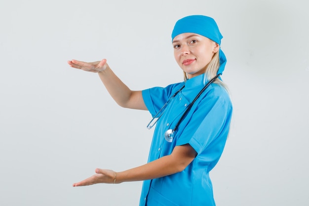 Vrouwelijke arts in blauw uniform die groot formaatteken toont en vrolijk kijkt