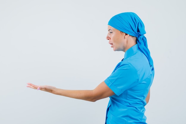 Vrouwelijke arts in blauw uniform die haar lege handpalm bekijkt en verbaasd kijkt.