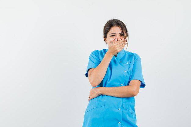 Vrouwelijke arts in blauw uniform die hand op mond houdt en gelukkig kijkt