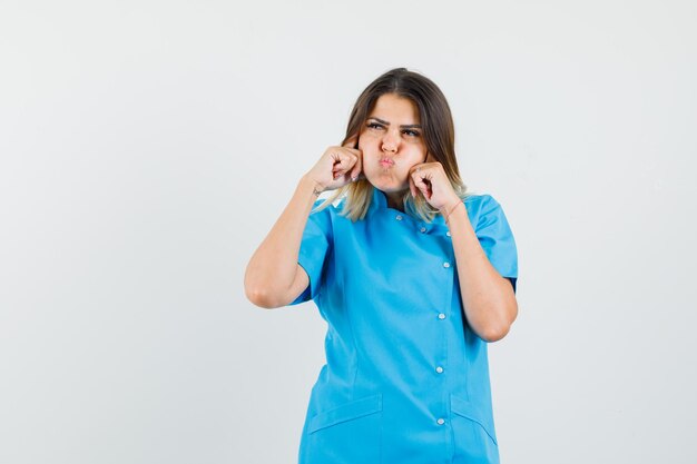 Vrouwelijke arts in blauw uniform die oren stopt met vingers, lippen pruilen