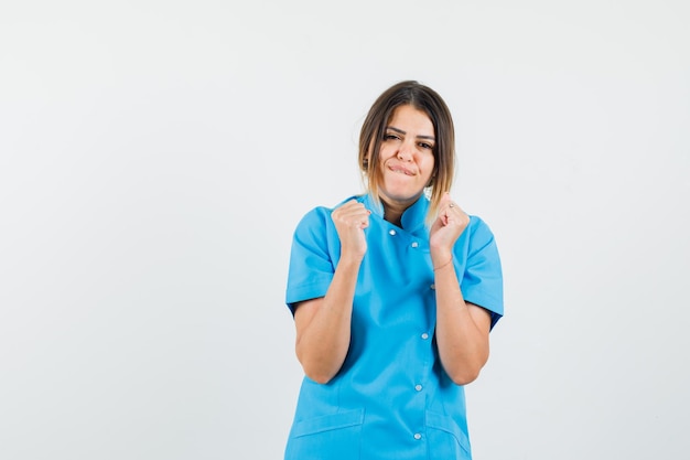 Vrouwelijke arts in blauw uniform die winnaargebaar toont en er gelukkig uitziet